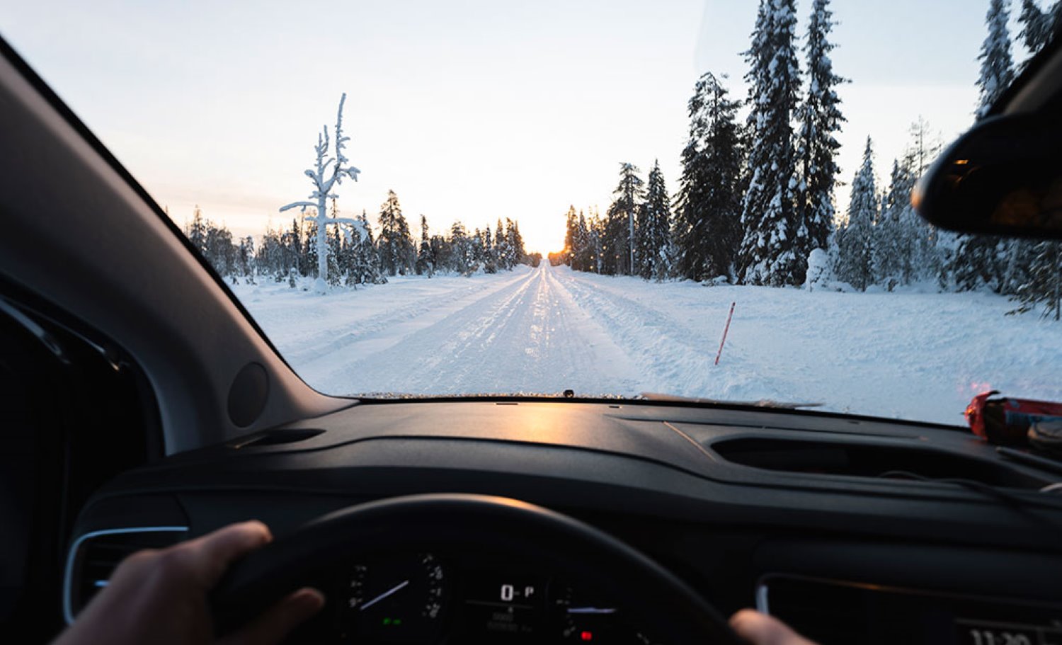 henkilö ajaa lumista tietä auringon laskiessa