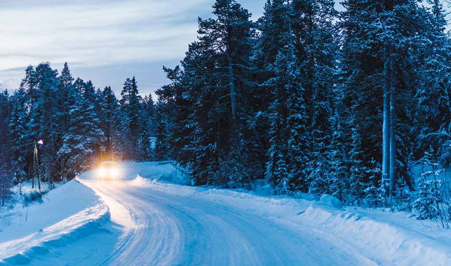 Auto ajaa lapissa lumista tietä valot päällä